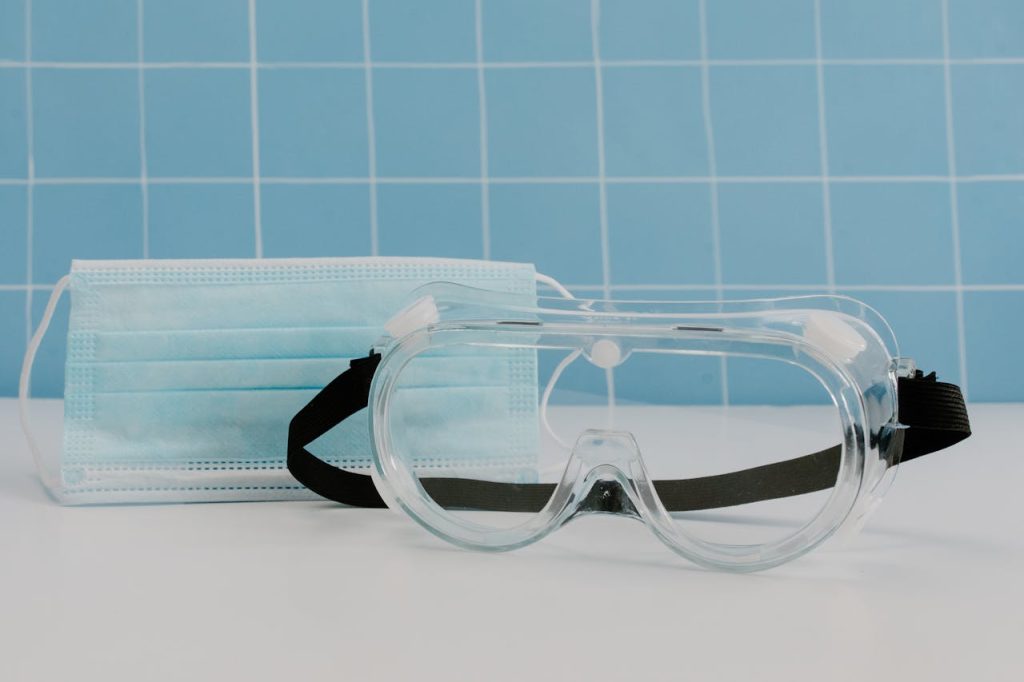 Close-up of protective goggles and a medical face mask against a tiled background.