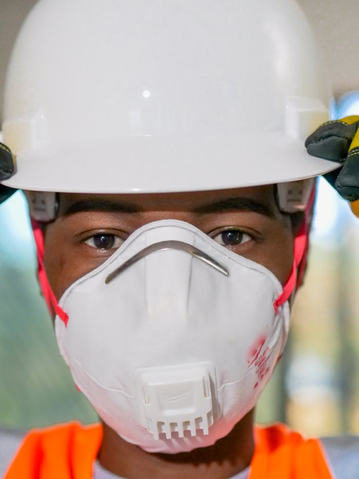 Close-up of a construction worker wearing safety gear, including a hardhat and N95 mask, for protection.
