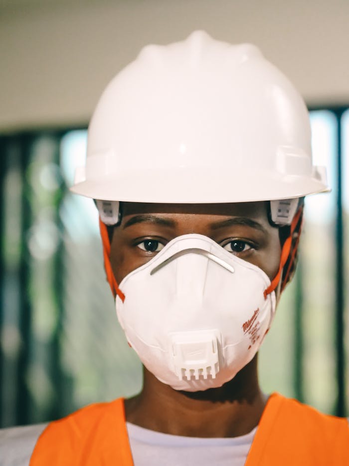 Close-up of a construction worker wearing a white hardhat and N95 mask indoors.